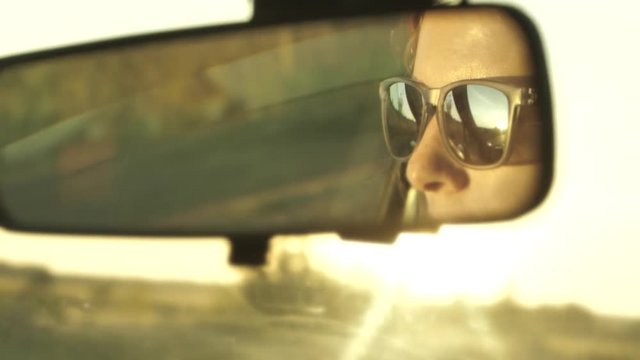 Women is driving a car on sunset. Reflection face in rear view mirror of vehicle.