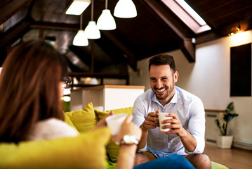 Couple in love enjoying their free time, sitting on a couch and drinking coffee.
