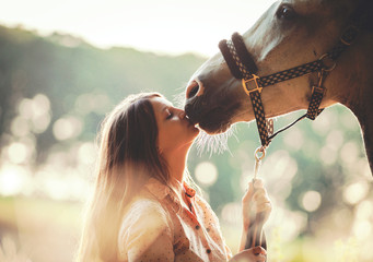 Woman kissing her horse at sunset, outdoors scene