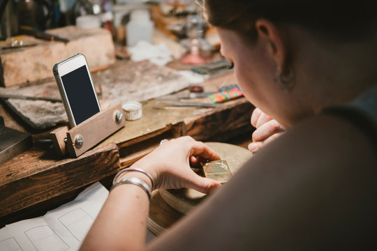 Over shoulder view of female jeweller engraving metal at workbench