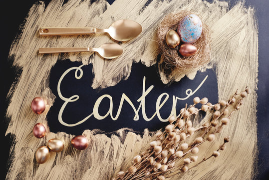 Overhead view of dyed and gold painted easter eggs and spoons with handwritten easter