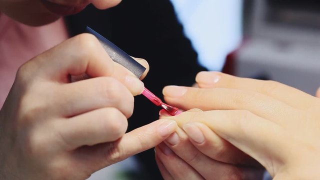 manicure making female hands, covering of transparent enamel and red nail varnish, nail polish.Woman hands in a nail salon receiving a manicure by a beautician. Woman getting nail manicure.