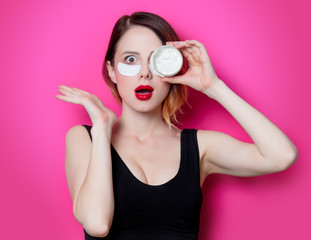 Woman using eye patch for her eyes and cream on pink background