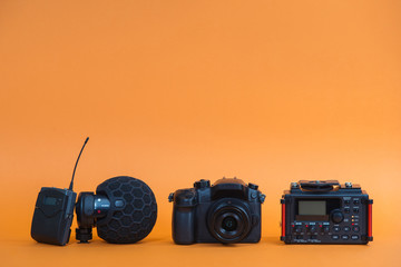 equipment for field video production, camera, microphone, recorder on orange background