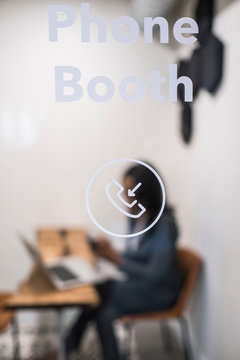 Businesswoman Sitting In Office Phone Booth, Using Laptop, Holding Smartphone, Differential Focus