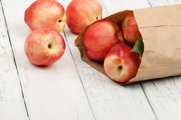 Ripe red peaches in the paper bag on the white wooden table