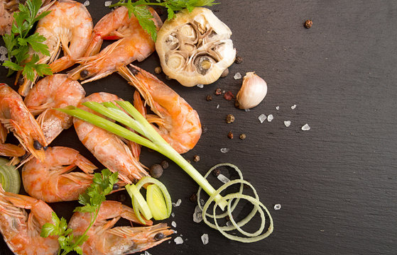 Bbq grilled shrimps on black slate serving with parsley, leek and baked garlic. Barbecue seefood concept. Healthy diet food. Top view.