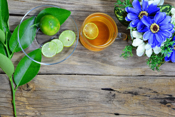 Obraz na płótnie Canvas top view of a cup of tea ,lemon sliced green lemon leaves and blue flower in vaase over old wooden table with space