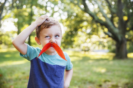 funny boy with a mustache from autumn leaves outdoors. child plays in the detective in the autumn park. the concept of intuition. Blurred background. Copy space for your text
