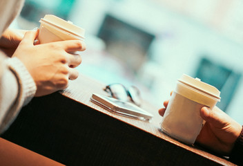 Two friends drinking coffee in paper take away cup - People having a break sitting in bar...
