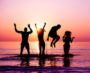 Silhouettes of happy friends jumping inside water on the beach at sunset - Group of young people having fun on summer vacation - Youth and friendship concept - Focus on bodies silhouette