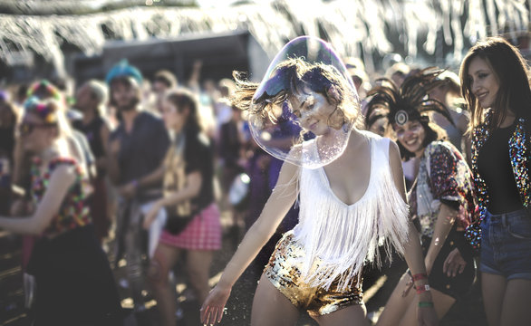 Young woman at a summer music festival wearing golden sequinned hot pants, dancing among the crowd.