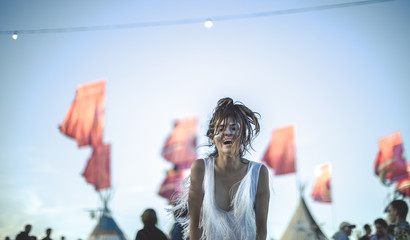 Young woman at a summer music festival face painted, smiling at camera, red flags in background.