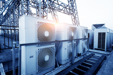 Air conditioner units (HVAC) on a roof of industrial building with blue sky and clouds in the...