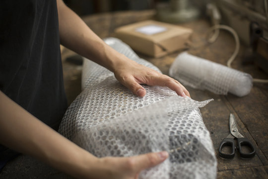A woman wrapping an item in bubble wrap, a parcel being prepared for despatch.