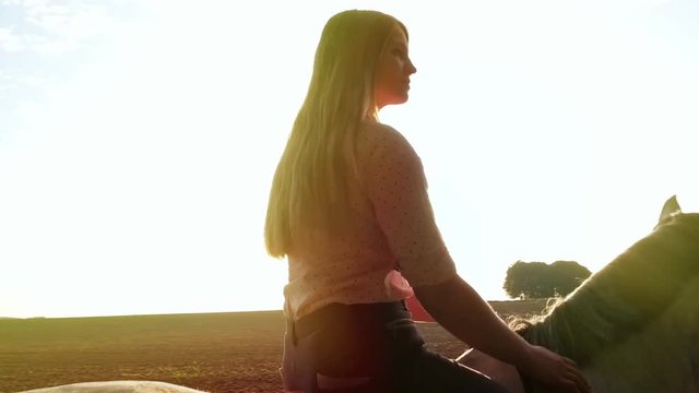 Young woman riding horse on country field during sunset, slow motion