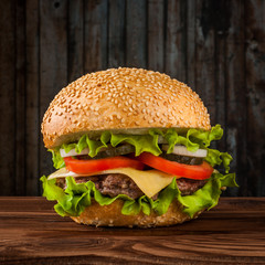 Delicious cheeseburger with salad ingredients on a grilled beef patty on a rustic wooden table with copyspace