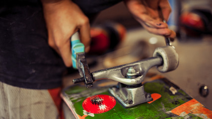 Young man in carpentry workshop fixing wheel on his skateboard