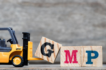 Yellow plastic forklift hold letter G to complete word GMP (Abbreviation of Good Manufacturinc Practice) on wood background