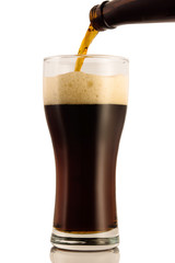 Dark beer poured into a glass from a bottle, isolated on a white background