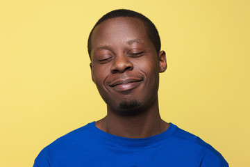 Satisfied young black man. Happy mood yellow background. Pleased African American guy, happiness concept