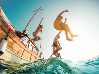 Happy friends diving from sailing boat into the sea - Young people jumping inside ocean in summer excursion day - Vacation, youth and fun concept - Main focus on left man - Fisheye lens distortion - obrazy, fototapety, plakaty