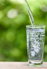 Pouring fresh water into glass on wood table with green nature background