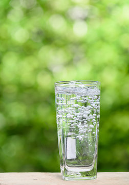 Glass of splash water on wood table with green nature background