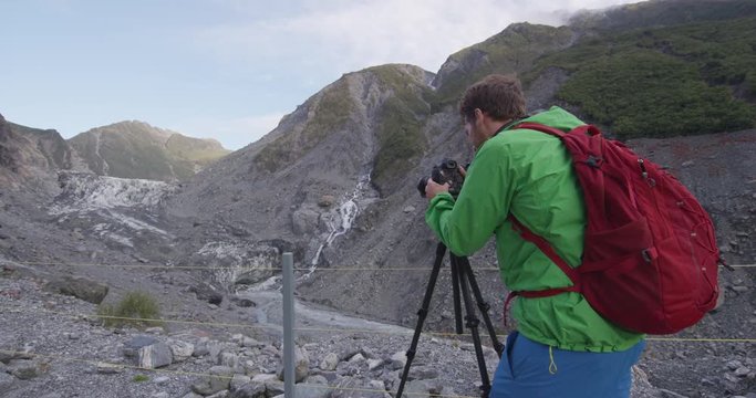 Photographer taking photos of Franz Josef Glacier in New Zealand, South Island. Man tourist taking pictures using SLR camera by famous New Zealand nature landscape and tourist destination.