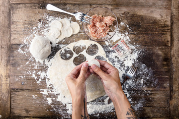 top view raw homemade dumpling in tattoed hands of housewife.  Process of cooking traditional russian cuisine at home. Flat lay top view