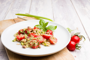 Vegetarian Quinoa salad with tomatoes, garlic,sunflower seeds and pistachios on a white plate on wood. Vintage white background