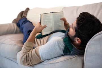 Man lying on sofa while reading book