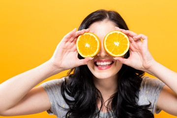 Happy young woman holding oranges on a yellow background