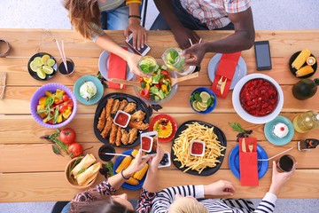 Top view of group of people having dinner together while sitting at wooden table. Food on the table. People eat fast food.