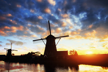 Landscape with beautiful traditional Dutch mill near water courses with fantastic sunset and reflection in water. Netherlands.