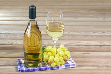 Bottle and glass of white wine are stand on table near bunch