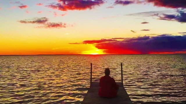 Frau auf einem Bootsteg an einem See bei Sonnenuntergang