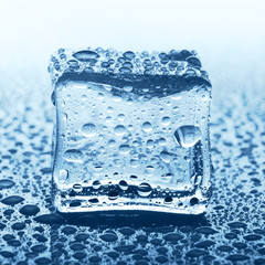 Transparent ice cube on blue glass with water drop