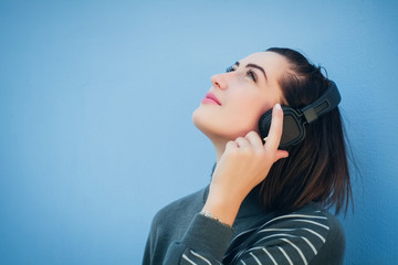 beautiful woman in headphones on blue wall background in gray dress, looking up