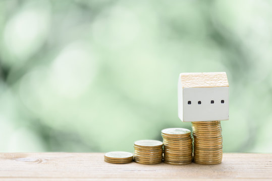 Saving money for house,stack coins and house model on wood table with pastel blurred background