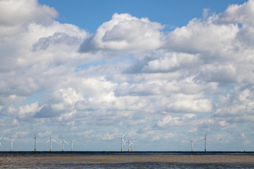 Offshore wind farm on horizon beneath cloudy sky.