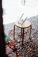 Fototapeta na wymiar Two empty glasses or jars of coffee, juice or lemonade with straws stand symmetrically on wooden table in front of cafe or bar in old town of dubrovnik