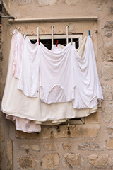 Fresh white clothes after wash and laundry hang dry on window shelf of old cobbled brick building in mediterranean european town or village, country life