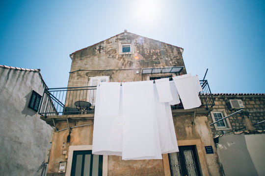 Bed sheets and covers fresh and wet hang to dry on rope on side of big old building, sunny sunday day with sun shinning bright