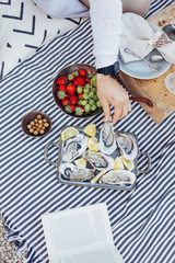 Man reaches out to vintage metal tray with fresh oysters, to try exquisite and luxurious seafood, on picnic blanket or restaurant table decorated in chic or bohemian style