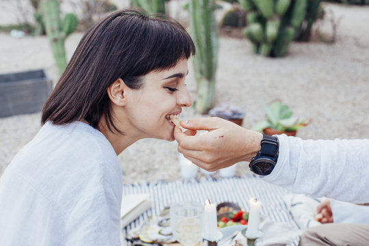 Couple enjoys picnic on fresh air together. Man feeds girlfriend or wife or partner from his hands, cheese or other tasty snack. Beautiful romantic date setup