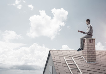 Handsome man on brick roof against cloud scape reading book