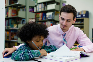 Portrait of teacher assisting little boy with homework in the library
