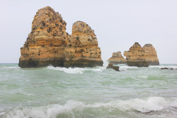 Natural cliff rocks standing isolated in the sea water during starting storm. Foggy unclear background, bad weather conditions, with small waves around beautiful stone cliffs on empty copy space.