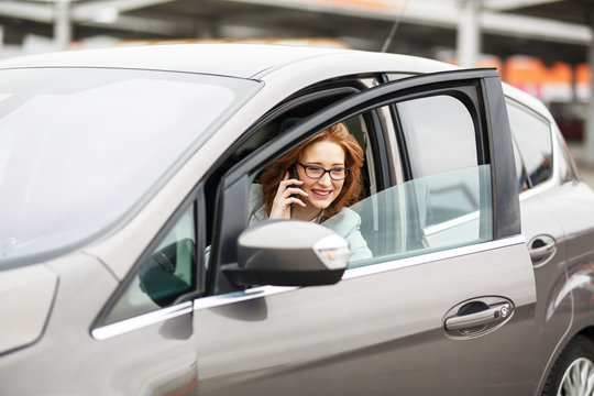 Attractive red hair businesswoman getting out of car and talking on phone.